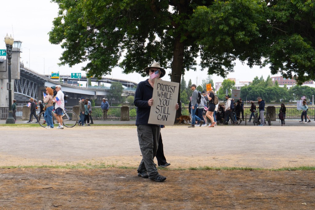 protester with sign "Protest while you still can"