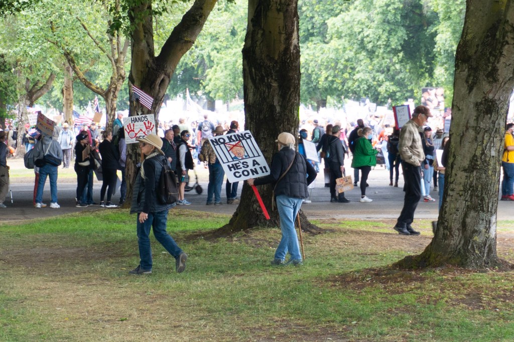 Elderly protester joining the growing crowd at the waterfront with a creative sign.